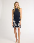 Woman modeling a black dress with white fern detailing on a white backdrop