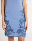 A woman wearing a hand-crochet blue dress with blue floral embroidery on a white background