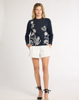 Woman wearing a black long sleeve sweater with white fern detailing on the front on a white backdrop