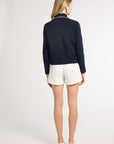 Woman standing to the back modeling a black hand-crochet jacket with white shorts on a white backdrop