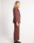 A woman modeling a matching two-piece suit in a dusty rose-brown color with a thin tan windowpane plaid pattern, shown from a side profile against a light gray studio background.