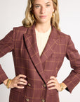 A woman wearing a double-breasted blazer in a dusty rose-brown color with a tan windowpane plaid pattern, styled over a cream cable-knit top.