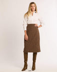 Woman with hand on hip wearing a white shirt, brown plaid skirt, and brown boots on a white background