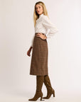 Profile of woman wearing white button-up shirt and brown plaid skirt with brown boots against a white background