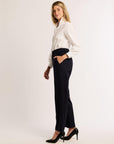 Profile of woman wearing a white blouse and navy pants with black heels on a white background