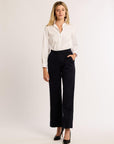 Woman wearing a white blouse and navy pants on a plain background