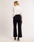Back of a woman wearing a white blouse with navy pants and black heels on a white background