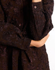 Close-up of a woman wearing a brown brocade dress with long sleeves.
