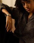 Person wearing a houndstooth patterned outfit with a watch, sitting against a neutral background.