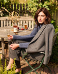 Woman sitting outdoors at a table with drinks, wearing a gray coat and blue sweater.
