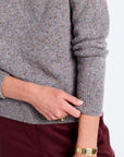 Person wearing a gray sweater and maroon pants with gold jewelry on a white background
