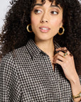 Portrait of woman wearing a flannel houndstooth patterned dress with gold hoop earrings and rings.