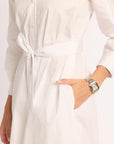 White dress with a belt and a hand wearing a watch on a light background