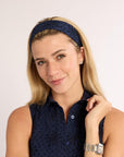 Woman wearing a navy headband and sleeveless top against a plain background