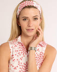 Woman wearing a white sleeveless top with red patterns and a headband on a plain background