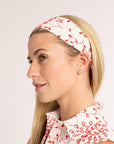 Woman wearing a white headband with red floral patterns on a plain background