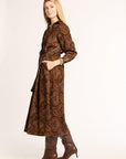 Woman wearing a long brown patterned dress with matching boots on a white background