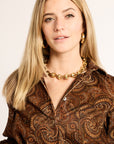 Woman wearing a patterned shirt and gold necklace against a plain background