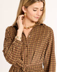 Woman wearing a brown checkered dress with gold jewelry on a white background