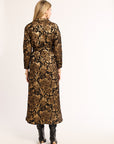 Woman wearing a long floral dress with a gold and brown pattern on a white background