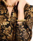 Person wearing a black and gold floral patterned outfit with jewelry.