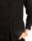 Close-up of a textured black jacket with a hand wearing a gold bracelet on a white background