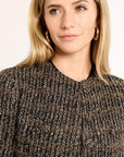Woman wearing a textured black and gold jacket against a plain background