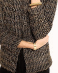 Close-up of a person wearing a textured brown jacket with gold bangles on a white background