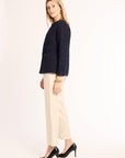 Woman wearing a navy jacket, beige pants, and black high heels on a white background