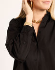 Person wearing a black shirt with gold jewelry on a light pink background