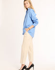 Woman wearing a light blue shirt, beige pants, and black high heels on a white background