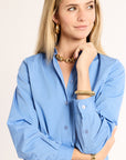 Woman wearing a blue shirt with gold jewelry on a beige background