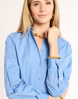 Woman wearing a light blue shirt with gold jewelry on a beige background