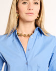 Woman wearing a blue shirt and gold necklace against a plain background