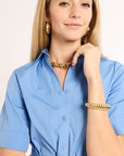 Woman wearing a blue shirt with gold jewelry on a beige background