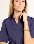 Woman wearing a navy dress with gold jewelry on a plain background