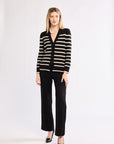 Woman wearing a black and white striped cardigan with black pants on a white background also wearing heels