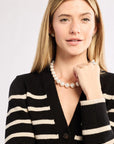 Woman wearing a black and white striped cardigan with a pearl necklace on a light background