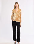 Woman wearing a striped beige cardigan with black pants on a white background wearing pearls