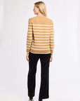 Woman wearing a beige and white striped sweater with black pants and heels against a white background