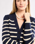 Woman wearing a navy and white striped cardigan with a pearl necklace on a white background
