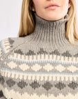 Person wearing a gray knit sweater with a patterned design on a plain background