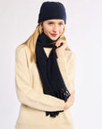 Woman wearing a navy beanie and scarf with a beige sweater on a white background