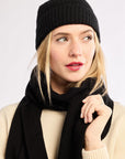 Woman wearing a black beanie holding a black scarf against a white background