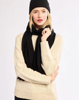 Woman wearing a black knit hat and scarf wearing a cream sweater on a white background