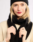 Woman wearing a black scarf, black beanie, and beige sweater on a white background
