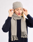 Person wearing a gray knit hat and scarf on a white background wearing a navy sweater
