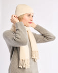 Woman wearing a beige knit hat and scarf with a gray sweater on a white background