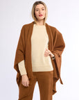 Woman wearing a brown poncho over a beige sweater and pants on a white background