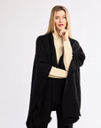 Woman wearing a black poncho over a beige sweater on a white background